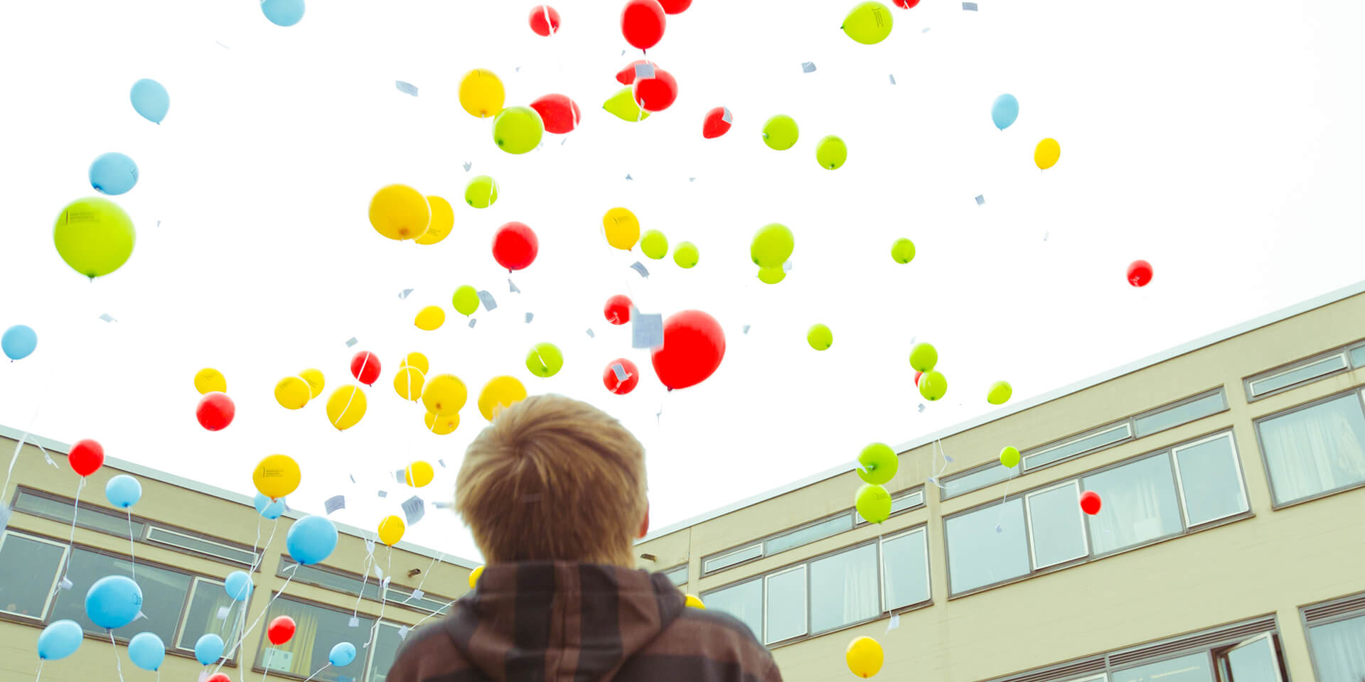 Ein Junge blickt in den Himmel voller Luftballons